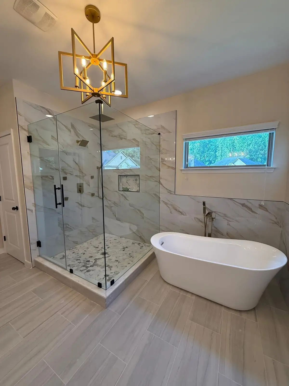 Luxury bathroom with frameless glass shower, freestanding tub, marble finishes, and gold chandelier in Fort Worth