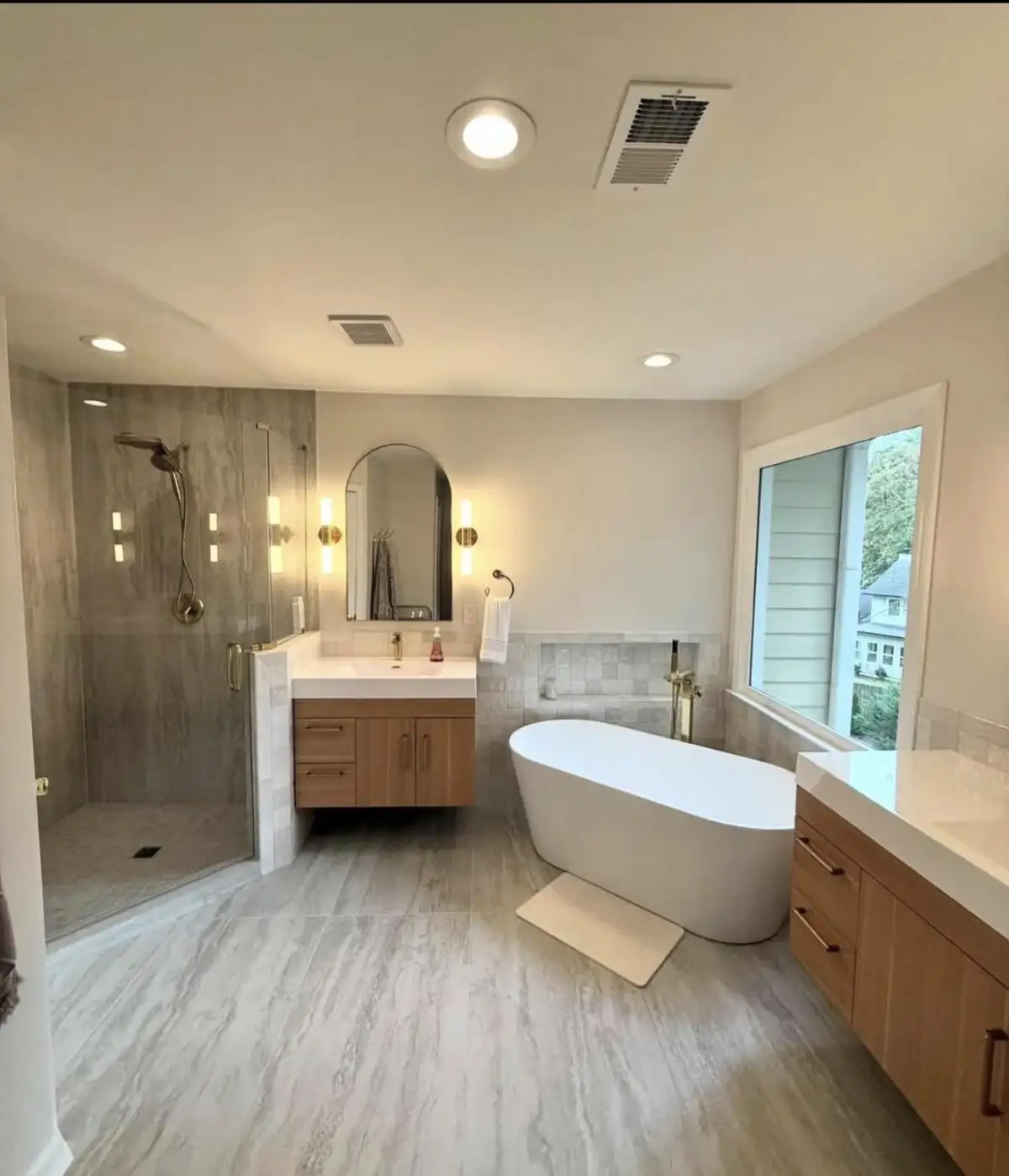 Master bathroom with freestanding tub, frameless glass shower, dual vanity, and arched mirror