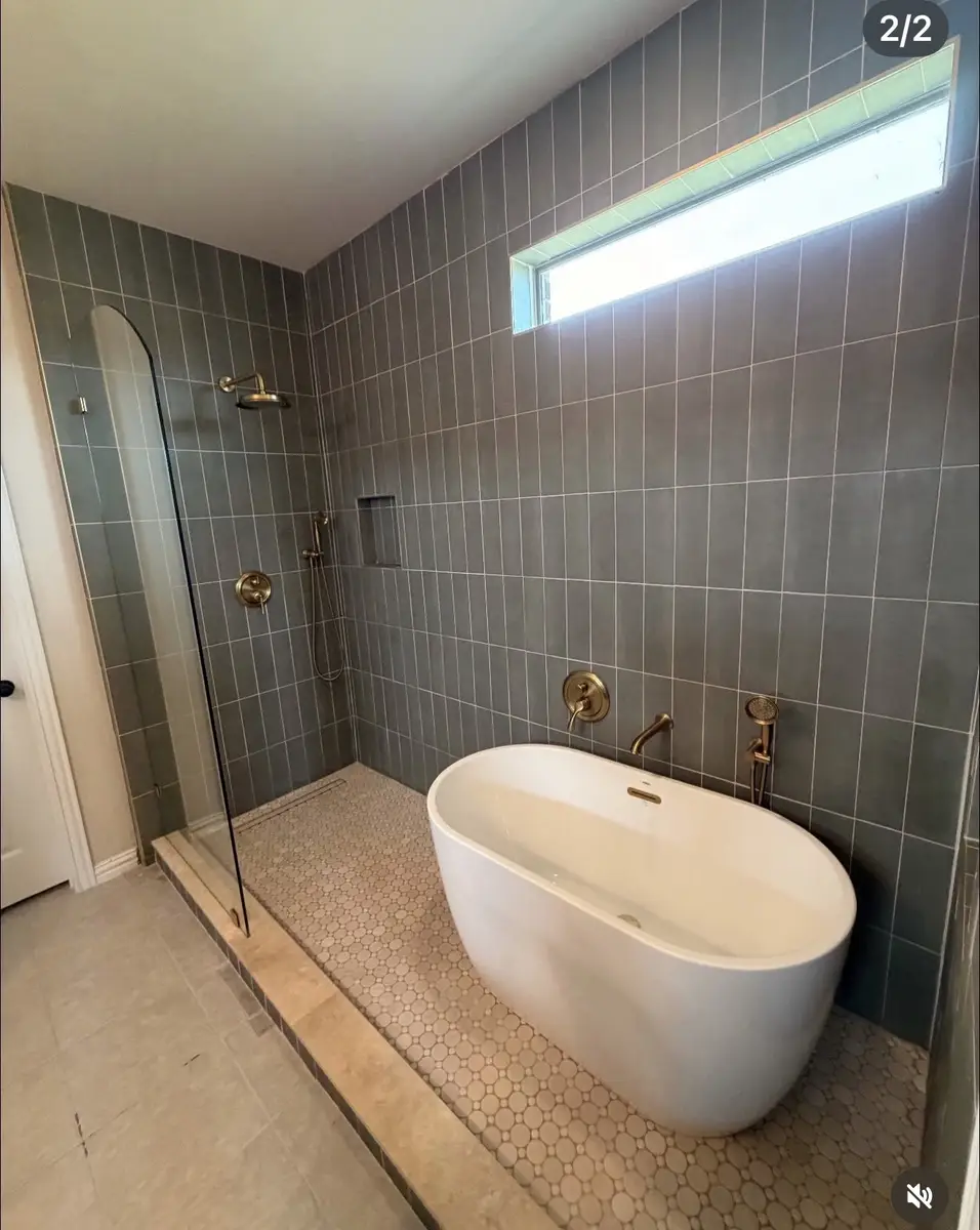 Completed luxury bathroom with freestanding tub, walk-in shower, gray vertical tile, and gold fixtures by Water and Stone