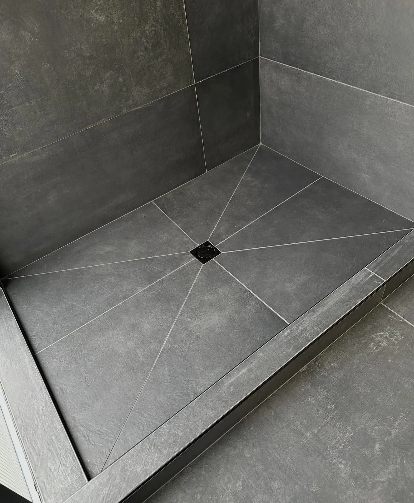 Dark tiled shower floor sloping to a central square drain