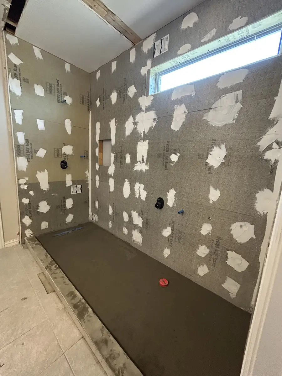 Walk-in shower during demolition phase with cement board, window, and exposed plumbing