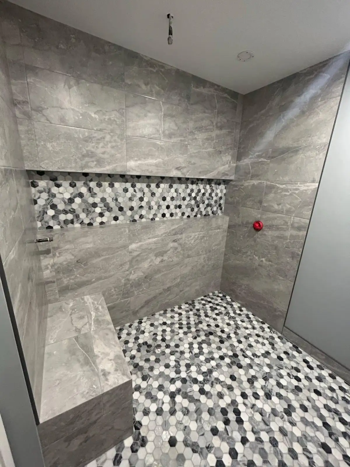 Gray stone tile shower with black and white hexagon mosaic floor and bench in Fort Worth