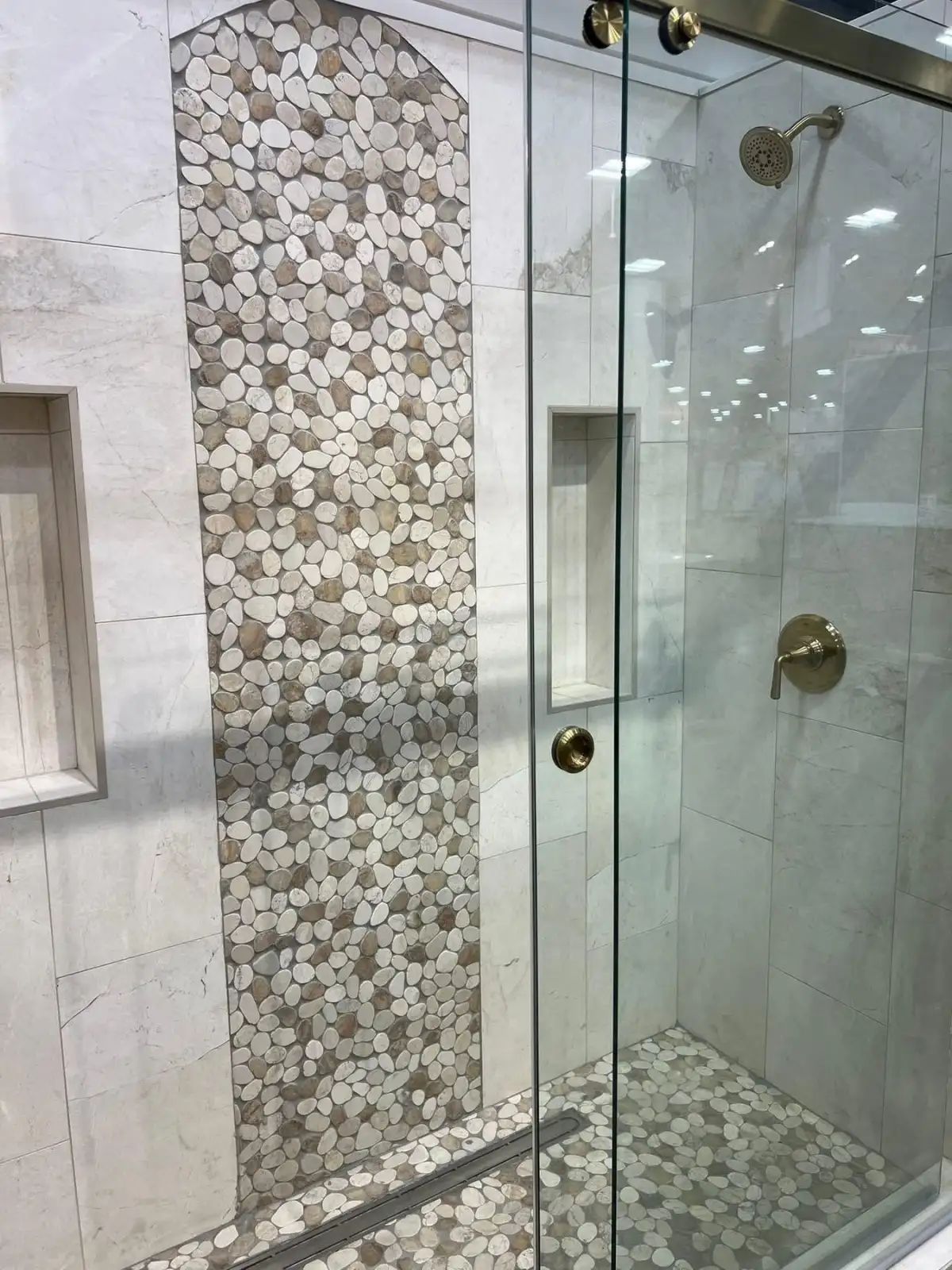 Marble tile walls with arched pebble stone accent, glass door, and gold hardware in Arlington bathroom