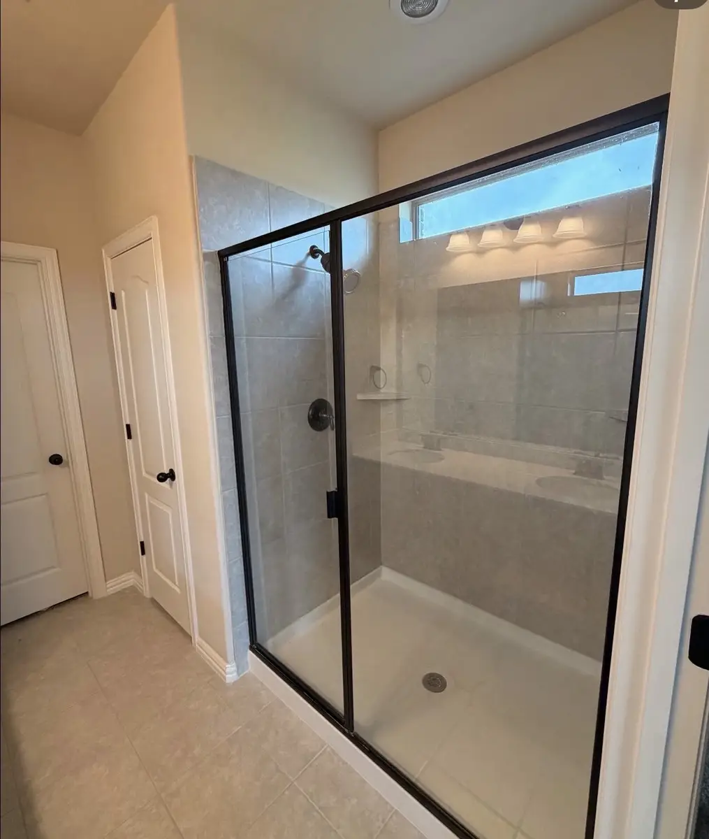 Custom walk-in shower with frameless glass door and oil-rubbed bronze fixtures completed by Water and Stone