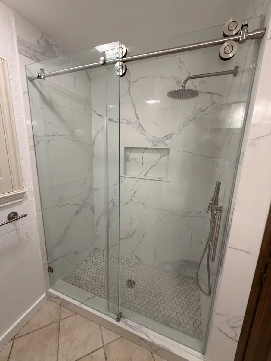 Walk-in shower with marble-look porcelain tile, sliding barn-door glass enclosure, and hexagon floor tile